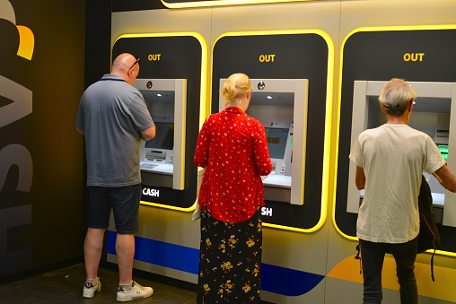 Antwerp city, Province Antwerp, Belgium - June 18, 2022: tourists one woman and 2 adult men taking money from the bank terminal in the underground basement railway station Leuven