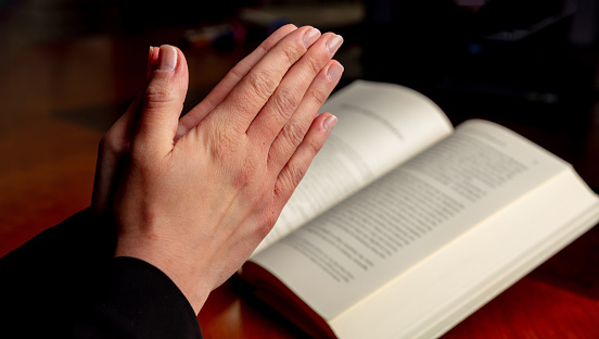 Pray to God, faith, religion and spirituality concept. Prayer, woman hands over an open Holy Bible book, wooden desk background.