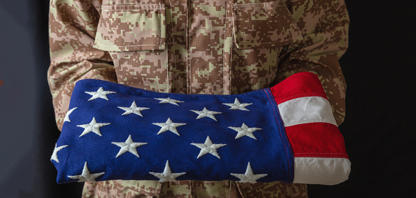 American army soldier in USA military digital pattern uniform, holds fold flag. United States, July 4th, independence day, camo uniform, US freedom.