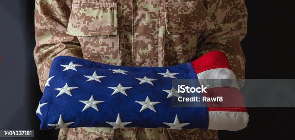 istock American army soldier in USA military digital pattern uniform, hold fold flag. July 4th. 1404337181