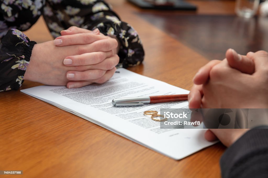Divorce signature, marriage dissolution document. Wedding ring and agreement on lawyer office table Signing a divorce, marriage dissolution documents and agreement. Wife and husband hands, wedding rings and legal papers for signature on a wooden table, lawyer office Divorce Stock Photo