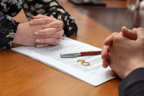 Photo of Divorce signature, marriage dissolution document. Wedding ring and agreement on lawyer office table