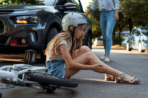 Little girl sitting on asphalt. Bicycle accident concept.