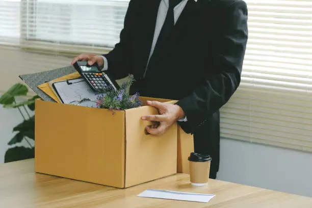 Photo of Resignation.Businessmen packing Stuff Resign Depress or carrying business cardboard box by the desk in the office. Quitting a job, The big quit. The great Resignation.Unemployment