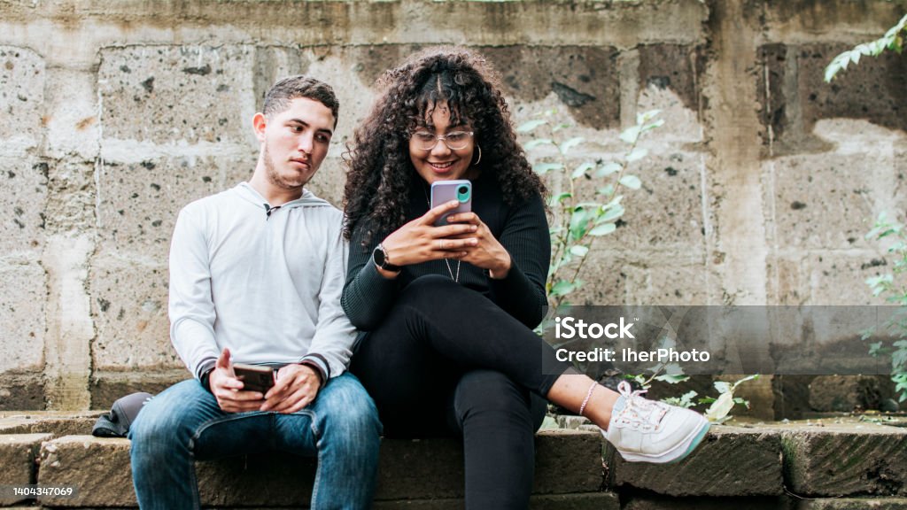 Suspicious person spying on his girlfriend phone, Jealous guy spying on his girlfriend phone, Distrustful boyfriend spying on his girlfriend phone Envy Stock Photo