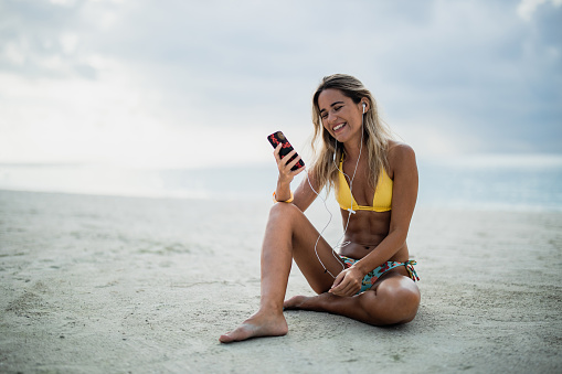 Happy woman enjoying in music over smart phone during summer day on the beach. Copy space.