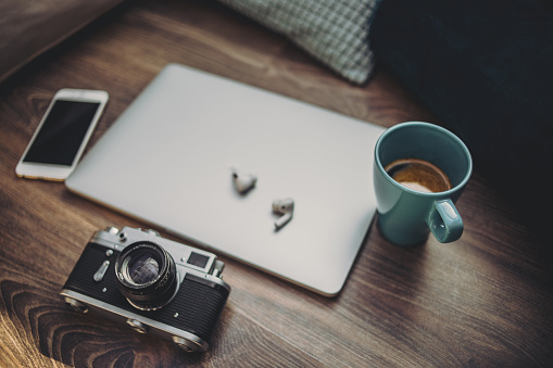 Coffee, laptop, headphones, mobile phone and camera on a wooden surface