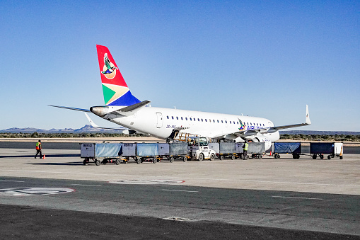 A commercial jet belonging to South Africa's Airlink Airline at Hosea Kutako International Airport of Windhoek in Khomas Region, Namibia. A person is visible in the background.