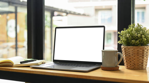 istock Computer laptop with blank display, potted plat, coffee cup and notebook on wooden table. 1404353382