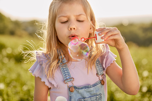 Caucasian girl playing with bubbles on the meadow