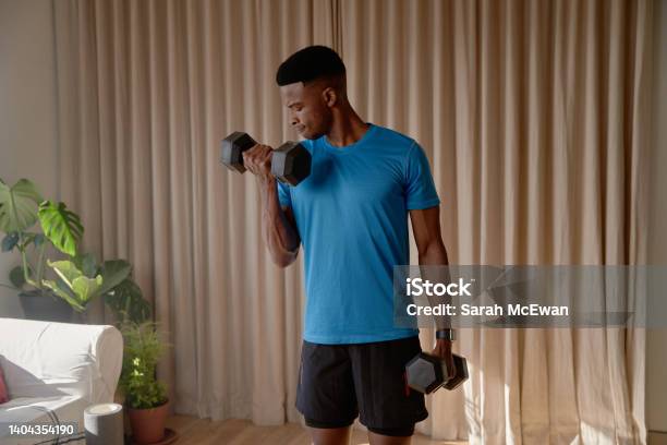 Young African American Black Male Working Out In Living Room At Home Doing A Bicep Curl With Heavy Dumbbell Weights Keeping Fit And Healthy With Strength Training Stock Photo - Download Image Now