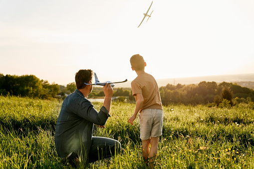 Little boy with dad playing toy airplane on the meadow