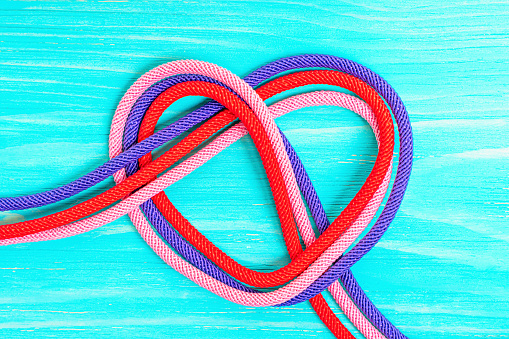 Heart symbol made of three multicolored cords twisted on a blue wooden background. Creative relationship concept.