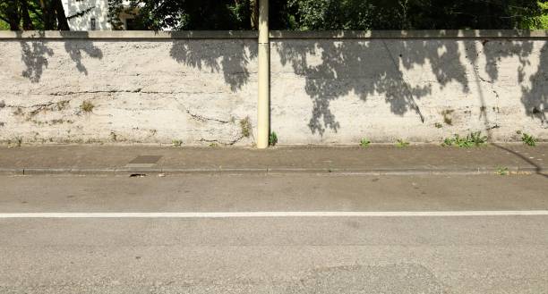 istock Grunge white plaster wall with plastic pole in the middle. Sidewalk and paved road in front, trees on behind. 1404365295
