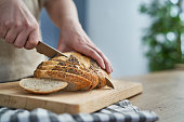Close up of woman cutting bread in slices on wooden board
