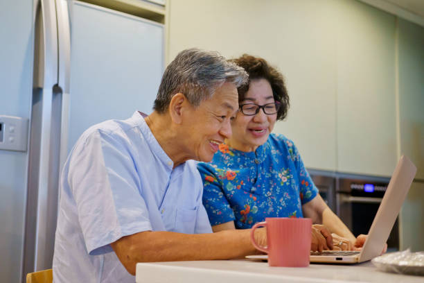 istock Senior Asian couple using laptop and smiling while preparing breakfast in the kitchen 1404365636