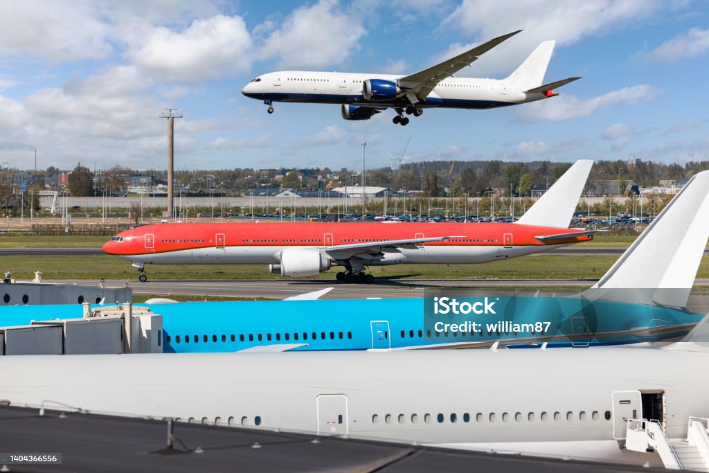 Busy airport view with airplanes parked, on taxiway and landing on runway Busy airport view with airplanes parked, on taxiway and landing or taking off on runway - Main airport hub with several aircrafts perfect for travel and industry concepts Airport Tarmac Stock Photo