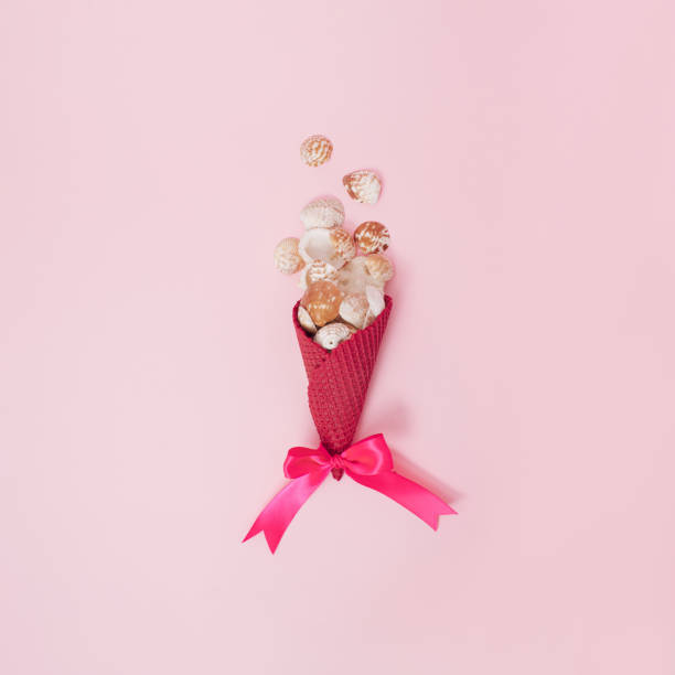 istock Rose colored ice cream cone with pink ribbon on the bottom filled with seashells on pastel pink background. Minimal vibrant sweet summer ice cream concept. 1404367329