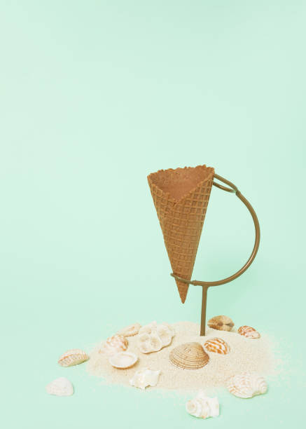 istock Ice cream cone on stand underneath decorated with sand and seashells on pastel green background. Minimal summer, vacation concept. Create layout with copy space. 1404367710