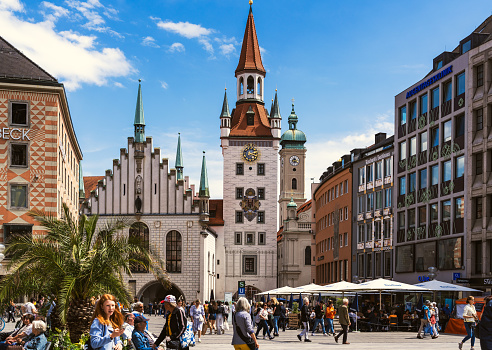 Marienplatz and Old Town Hall (Altes Rathaus) of Munich in sunny day. Marienplatz is the most important town square of Munich and is a pedestrian zone. Tourists and locals stroll in the square in front of the ancient monument.