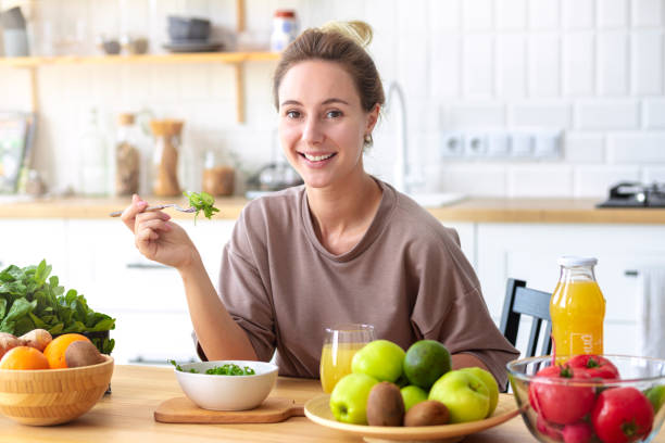 Healthy lifestyle, diet, weight loss concept Beautiful happy woman eats breakfast looking at the camera and smiling friendly Beautiful female eating fresh salad while sitting in kitchen Vegan meal stock photo