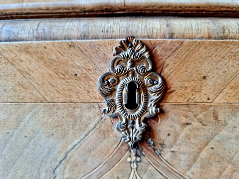 Antique decorated mettallic keyhole on a wooden door.