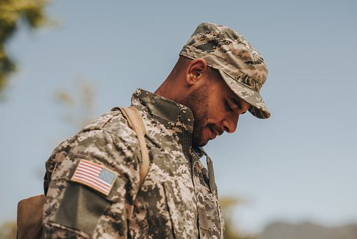 Brave young soldier looking down while standing outside his home. Patriotic American serviceman coming back home after serving his country in the military.