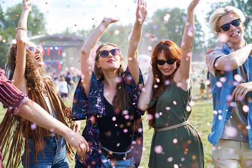 Group of caucasian young people dancing among confetti on music festival