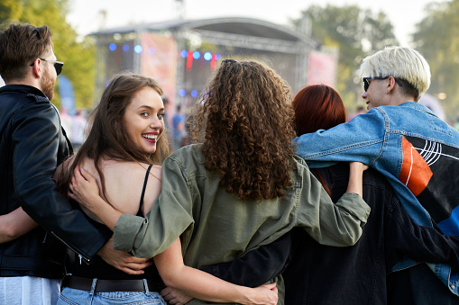 Group of young caucasian friends walking on music festival when one woman is turning toward camera