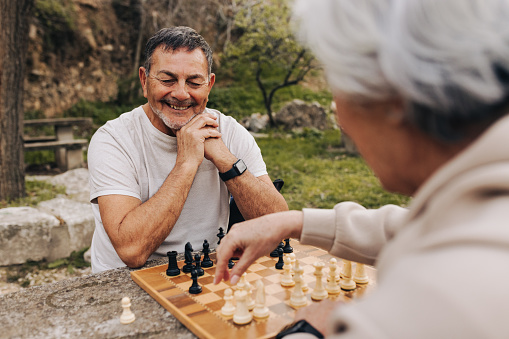 Mature couple playing a game of chess together in a park. Cheerful elderly couple spending some quality time together after retirement. Senior couple having a good time outdoors.