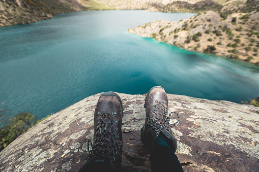 Woman hiker sit on cliff edge facing the beautiful high altitude lake