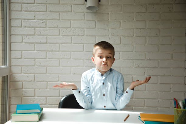 istock A schoolboy at a white desk shows a don't know gesture against a brick wall 1404382090