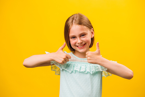 Like and approval. Studio portrait of stylish little children girl gesturing thumbs up and looking at camera. smiling to camera, yellow background