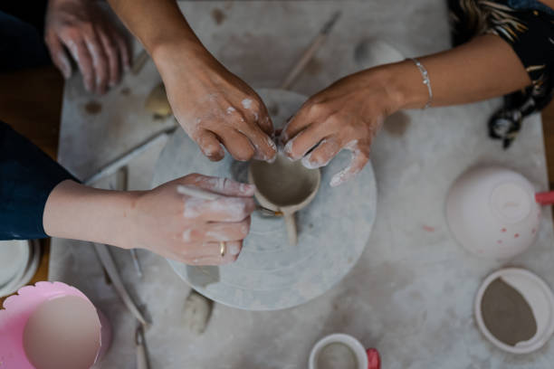 istock Beautiful instructor teaching woman to do pottery using a pottery wheel on a workshop 1404386569
