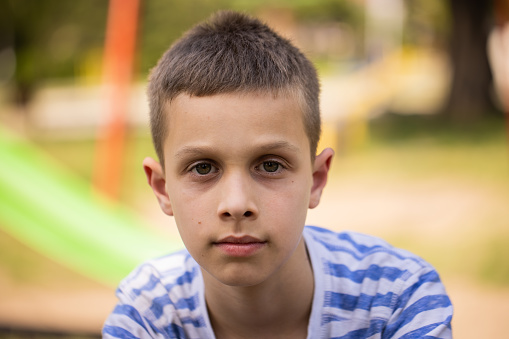 Portrait of Caucasian boy with contented emotion, sitting on the park bench