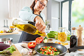 Woman adding cooking oil to a frying pan with vegetables