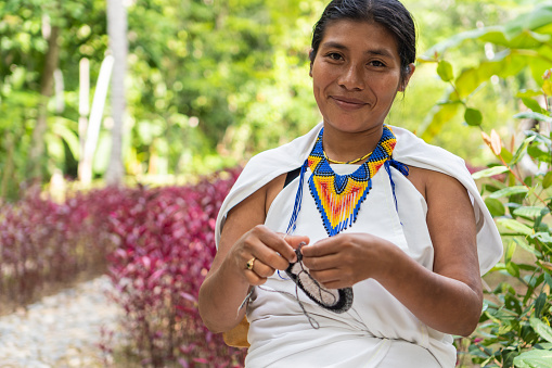 Mujer indígena con ropa tradicional tejiendo mirando a la cámara photo
