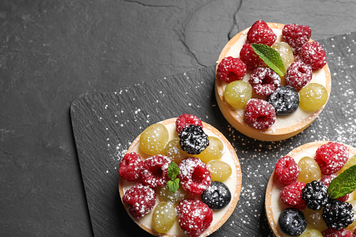 Delicious tartlets with berries on black table, top view