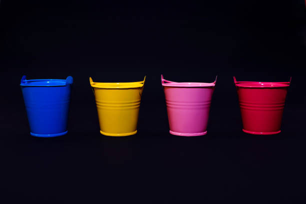 Four multi-colored buckets on a black background with place for text, blue, yellow, pink and red buckets, gardening concept, colorful on black