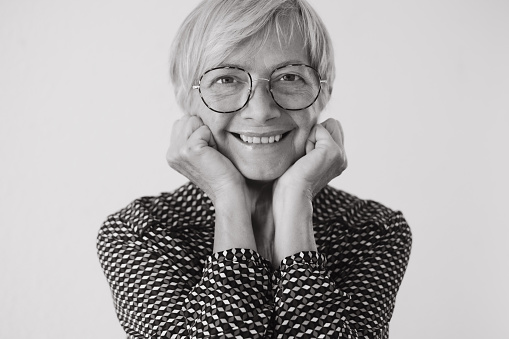 Black and white portrait of beautiful older woman wearing glasses looking at camera smiling. Short haired caucasian lady feeling in a good mood