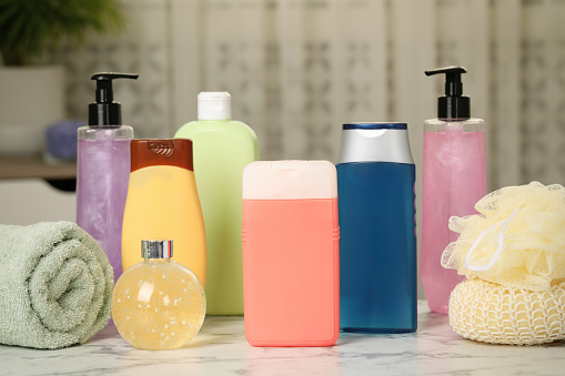 Bottles of shower gel, towel and sponges on white marble table in bathroom