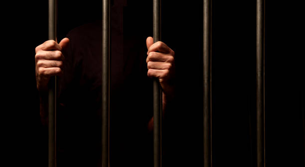 istock hands of a prisoner behind prison bars on black background 1404406747