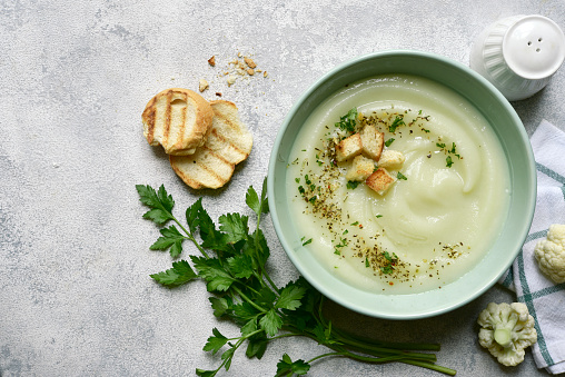 Vegetarian cauliflower cream soup with croutons  in a bowl over light grey slate, stone or concrete background. Top view with copy space.
