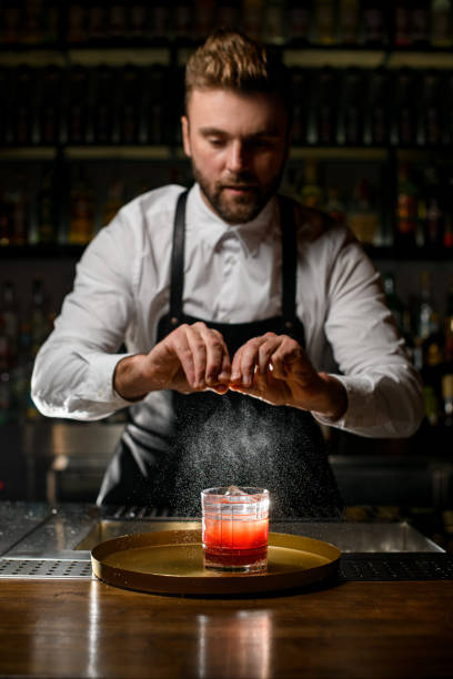 professional man bartender skillfully sprinkles by citrus peel on glass with cocktail professional man bartender skillfully sprinkles by citrus peel on a glass with a cocktail on a tray on the bar counter bartender stock pictures, royalty-free photos & images