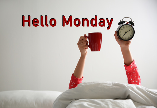 Hello Monday, start your week with good mood. Closeup view of woman with cup and alarm clock lying in bed