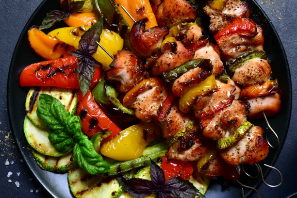 Chicken kebab skewers with grilled vegetables. Top view with copy space. Chicken kebab skewers with grilled vegetables on a dark slate, stone or concrete background. Top view with copy space. chicken skewer stock pictures, royalty-free photos & images