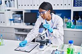 istock Young african american woman scientist using microscope write on document at laboratory 1404416774
