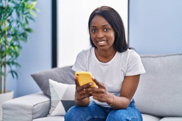 istock Young african american woman using smartphone sitting on sofa at home 1404416800