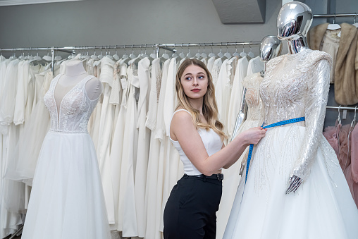 Designer woman's doing measurements elegant wedding dress in store