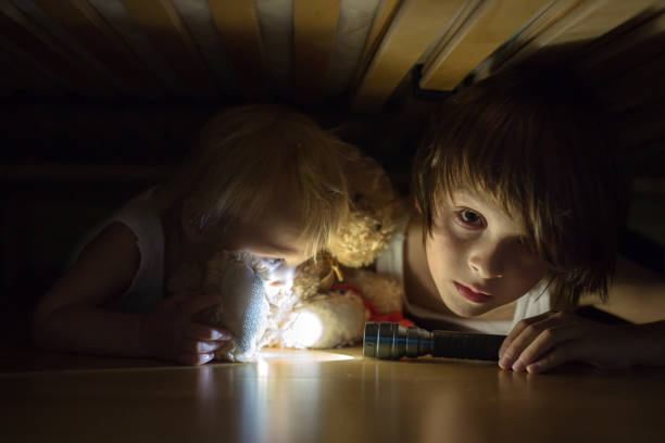istock Little child, hiding under the bed, hugging teddy bear and holding flashlight, 1404417455